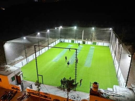 Aerial view of a caged floodlit cricket ground at night