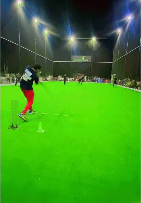 Player batting under floodlights on an indoor cricket ground at night