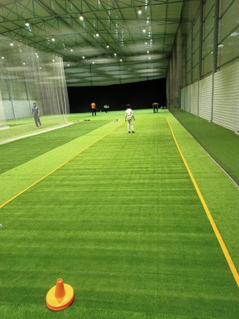 Indoor cricket practice lane with green astro turf and net cage